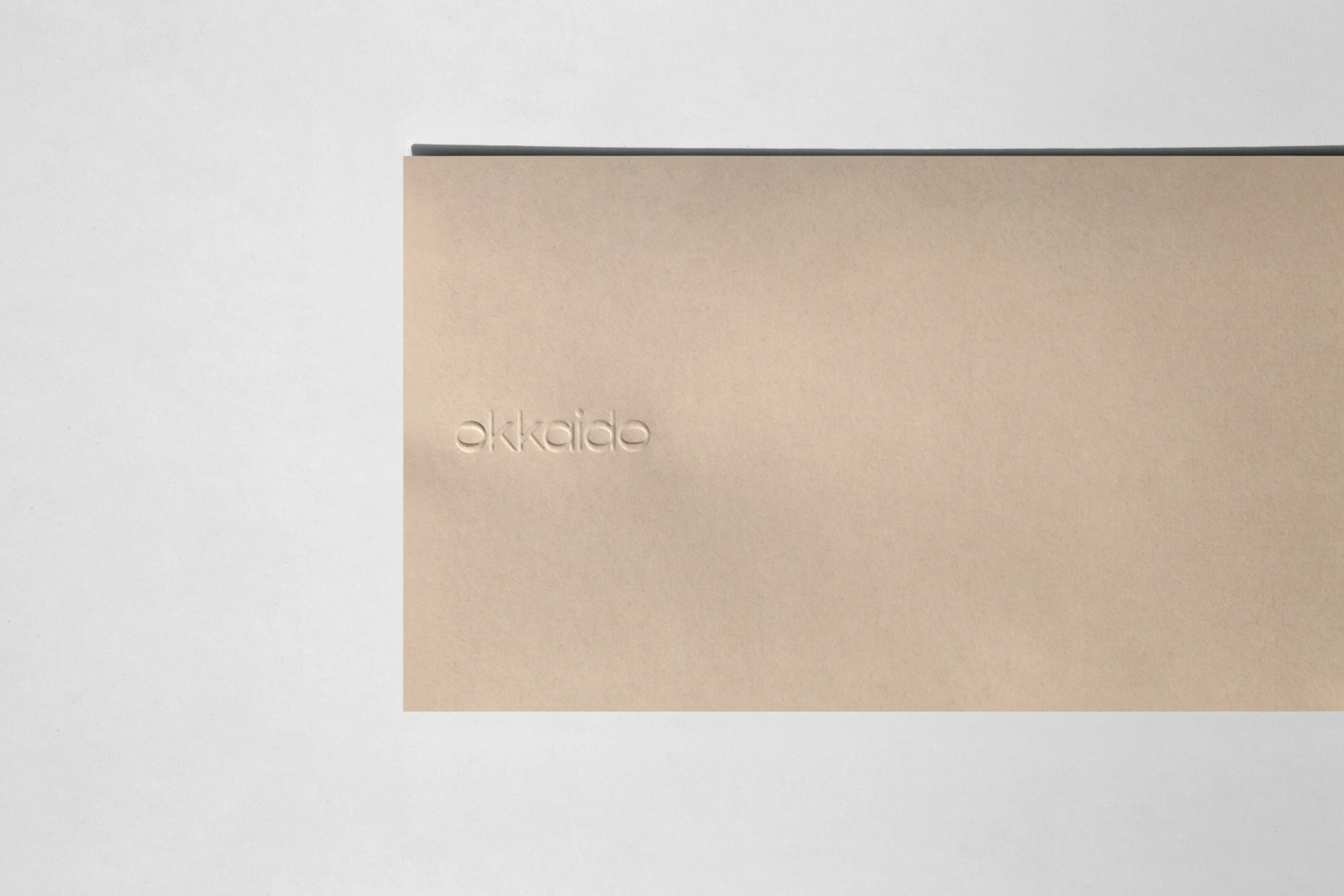 Beige textured paper card with an embossed Okkaido logo against a neutral light grey background
