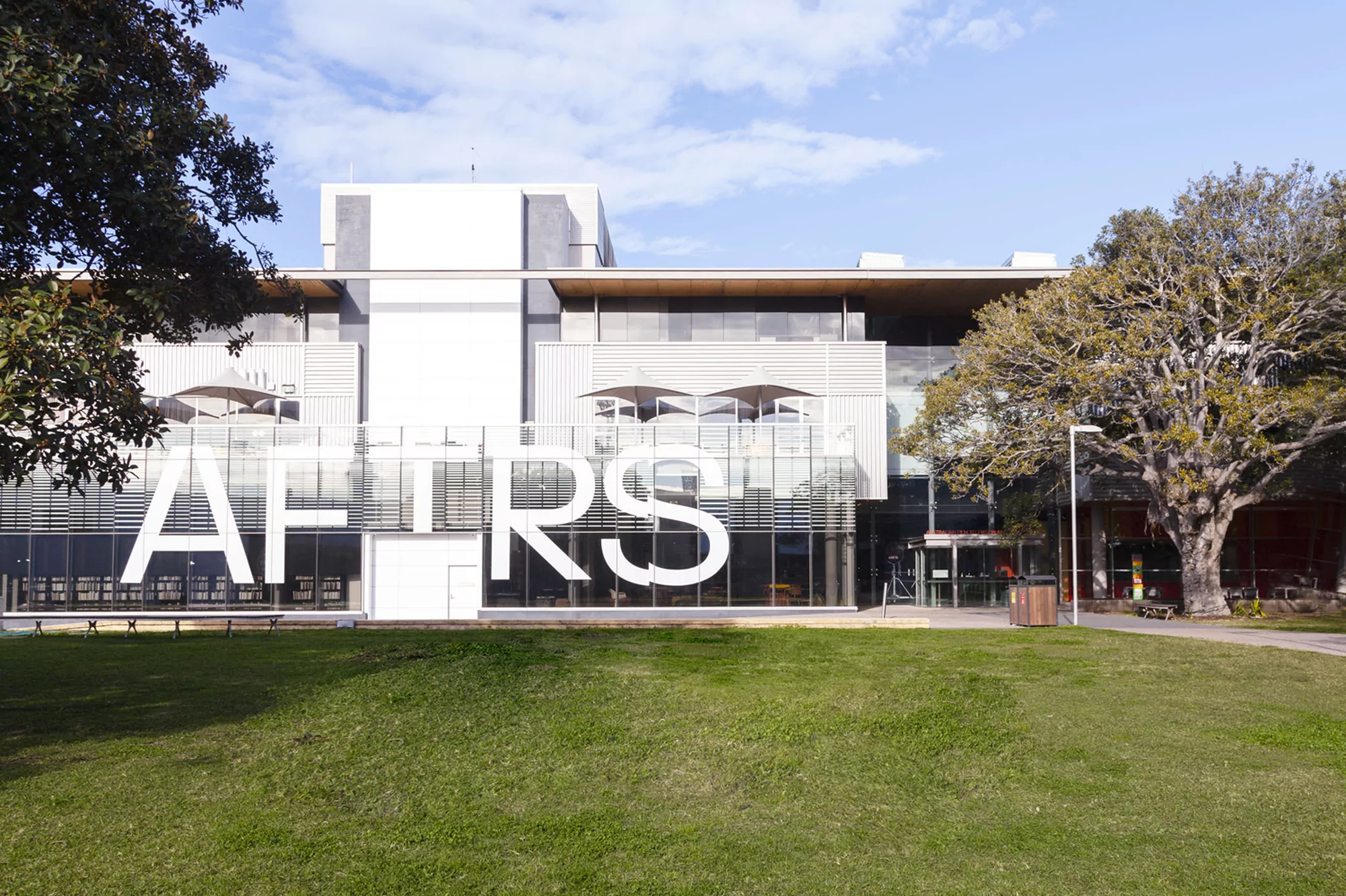Exterior view of the Australian Film Television and Radio School (AFTRS) building with a green lawn, blue sky, and mature trees.