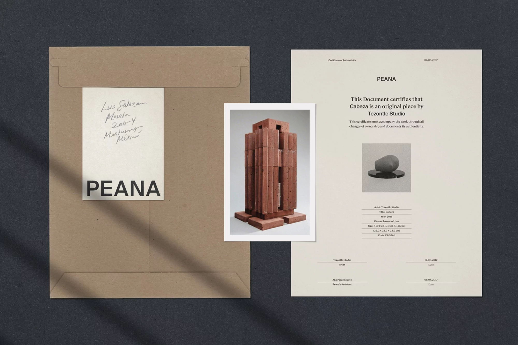 Still life featuring a tan envelope, an art print depicting a brick sculpture, and a certificate of authenticity against a dark background.