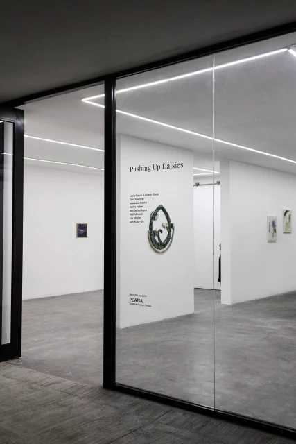 Art gallery exhibition featuring art pieces on display within a modern, minimalist space with white walls and glass door frames.