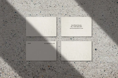 Four off-white business cards arranged on a speckled stone surface under harsh diagonal sunlight and shadows.
