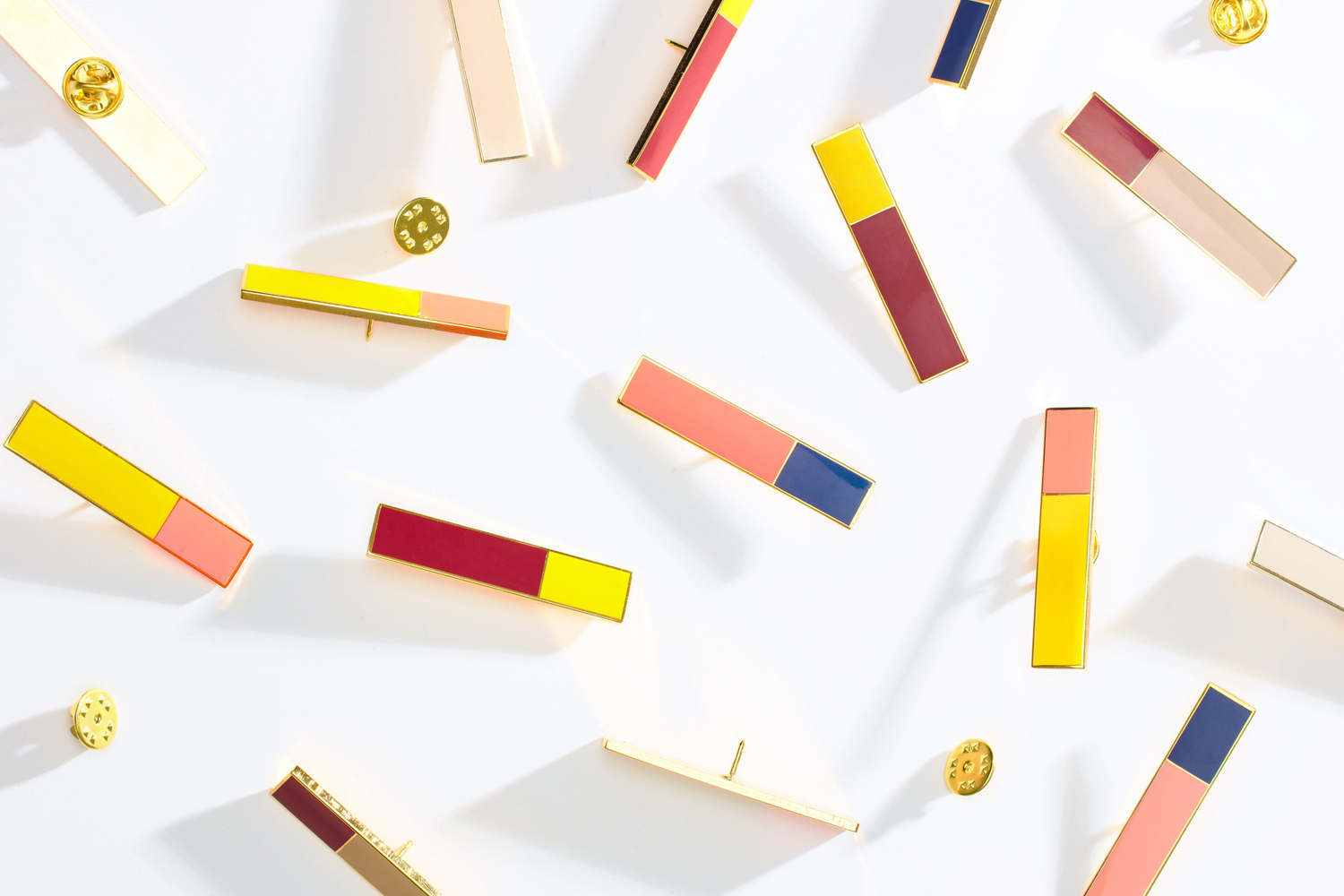Collection of colorful, enameled pin badges with geometric color block designs on a clean white background with soft shadows.