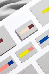 Flat lay of grey stationery cards with embossed colourful paper blocks on a white surface with fabric.