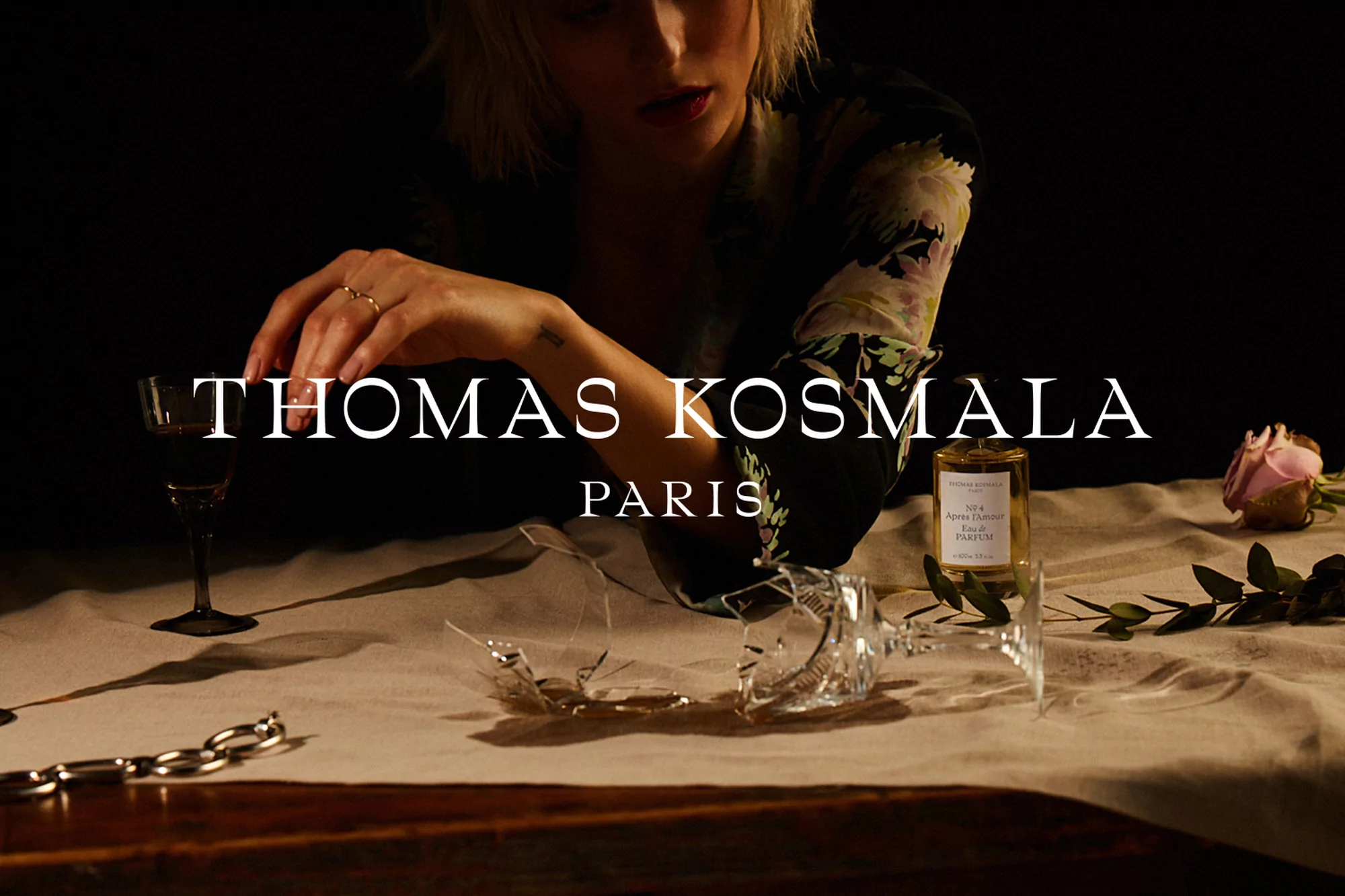 Elegant product shot featuring Thomas Kosmala perfume bottle with woman, rose, and fragmented glass, set against a dark, moody backdrop.
