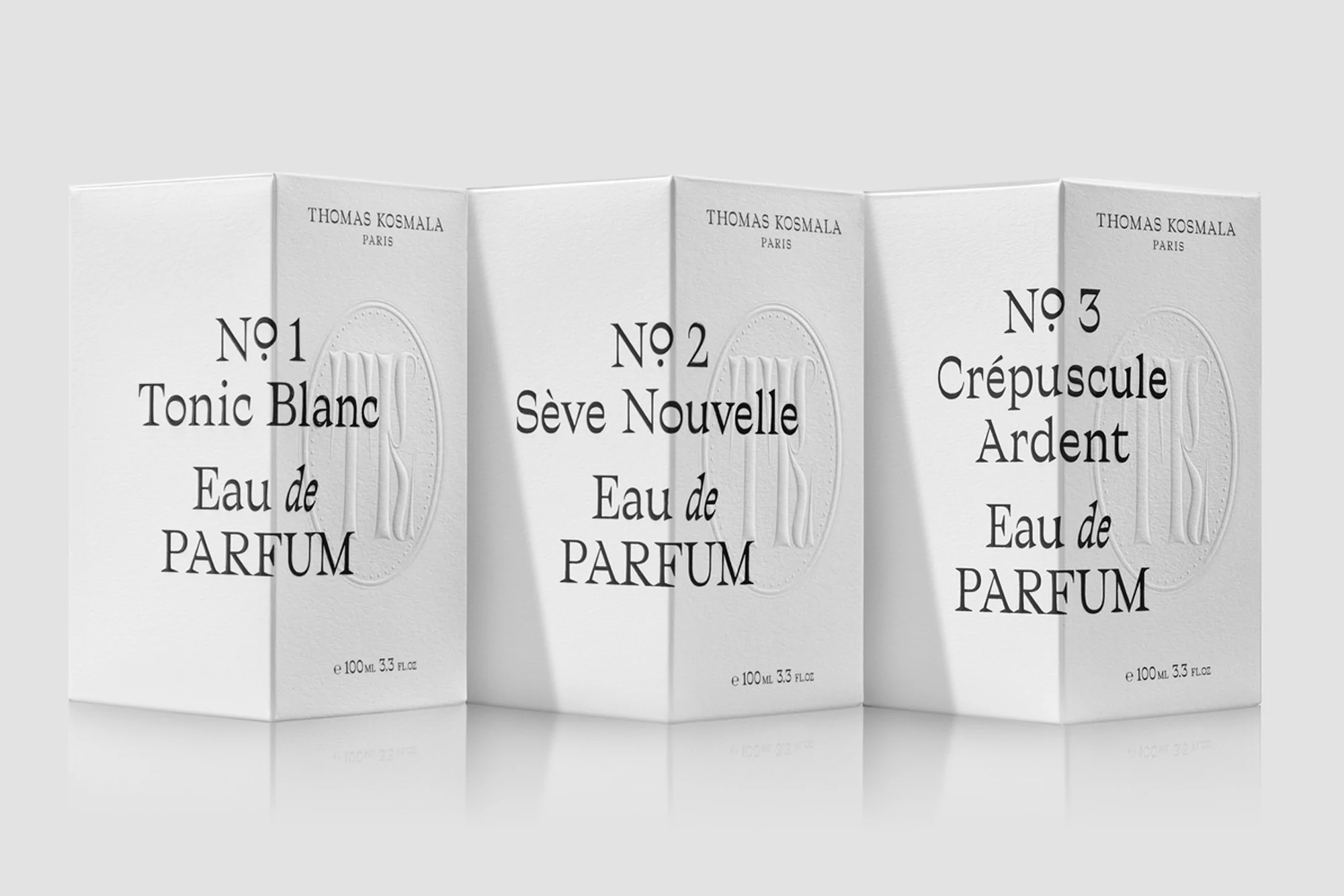 Three white Thomas Kosmala Paris Eau de Parfum boxes stand side-by-side with black text on a gradient gray reflective surface.