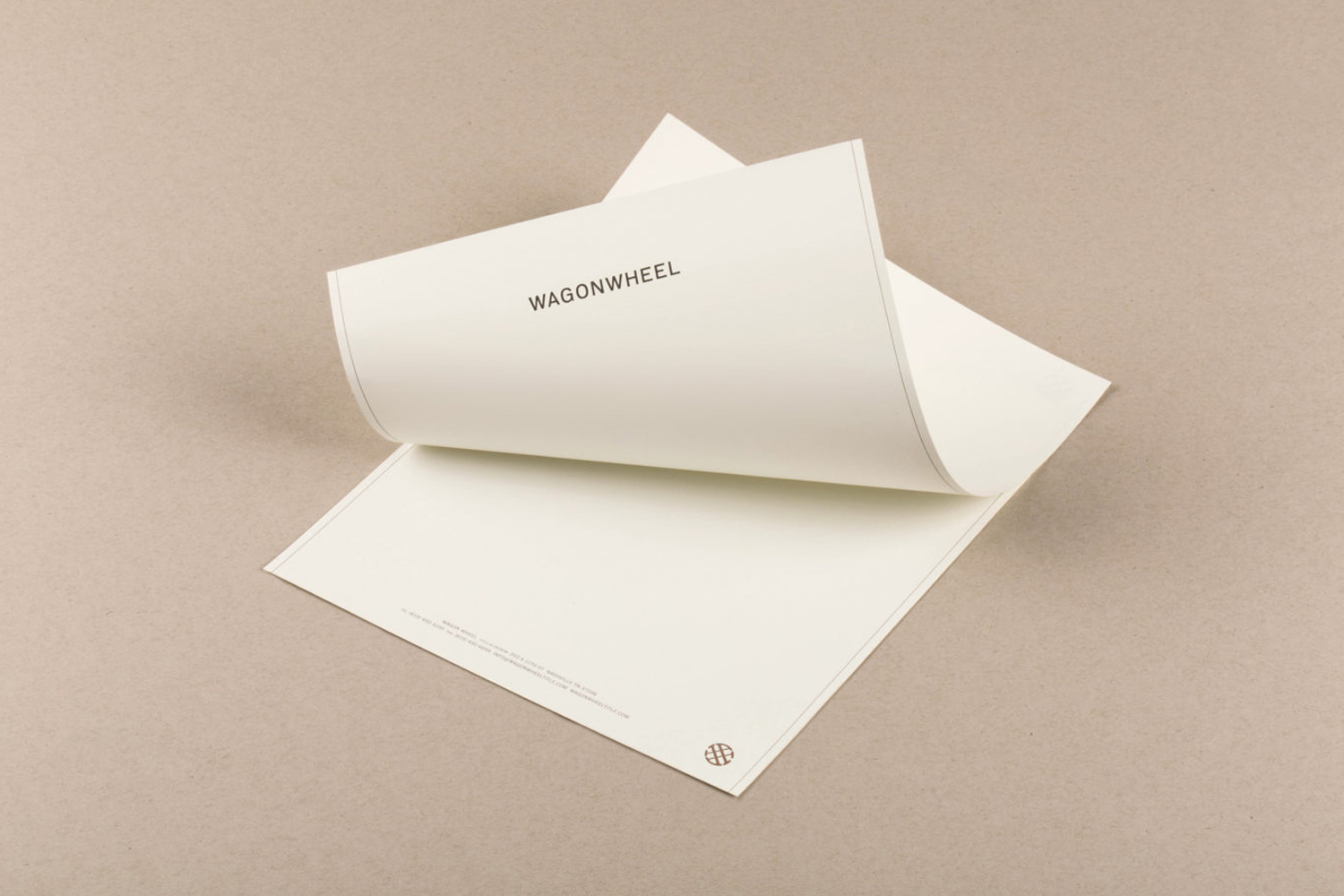 Image of two sheets of white paper with the text 'WAGONWHEEL' in a light neutral background. The top sheet is being lifted.