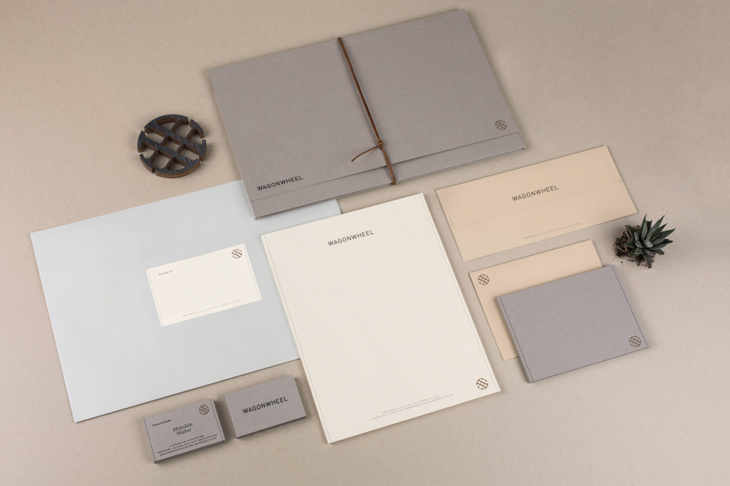 Arrangement of gray and cream-colored stationery, including envelopes, business cards, and a letterhead, alongside a small succulent.