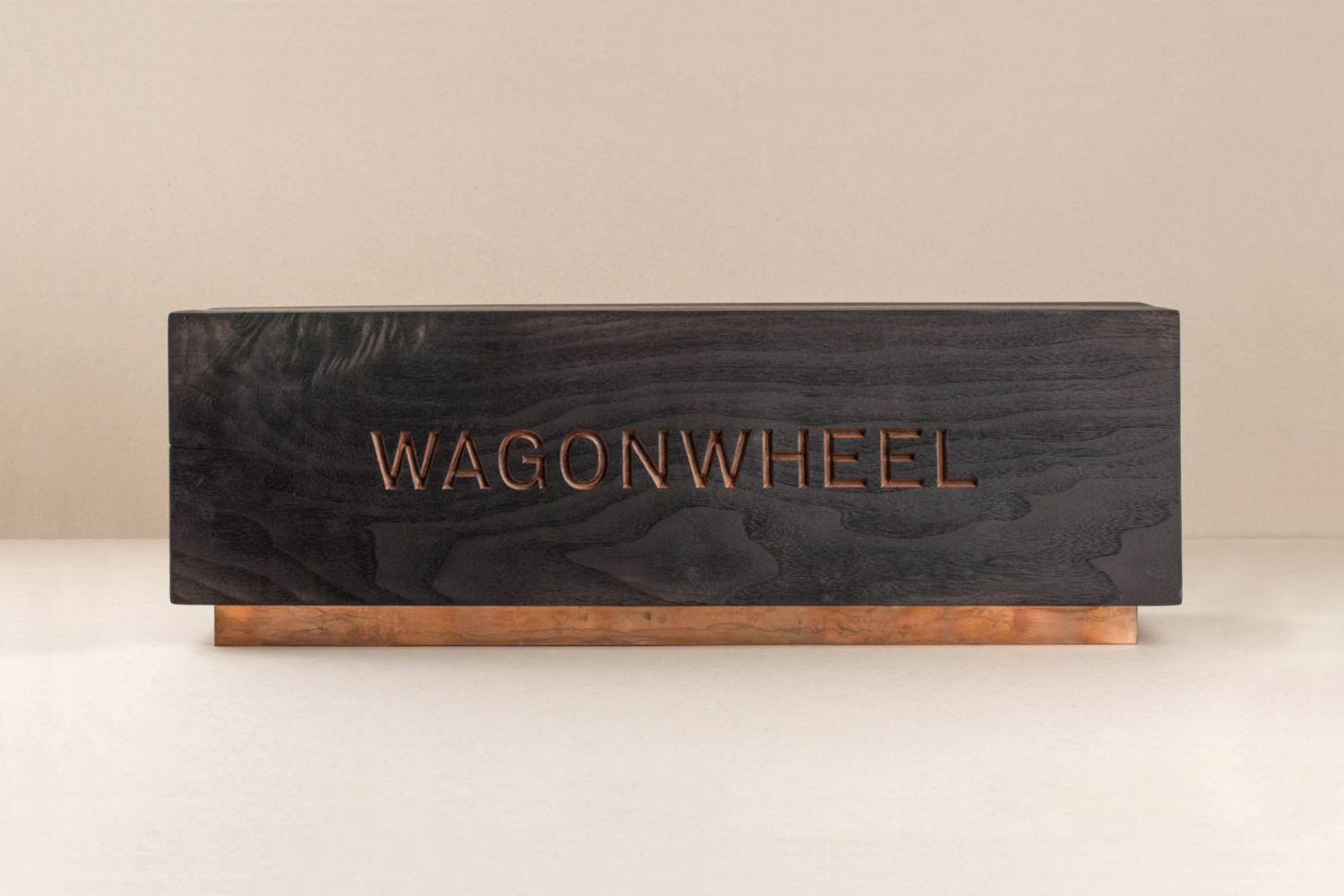 Rectangular dark wood box with copper base and 'Wagonwheel' engraved in the wood, minimalist studio lighting, and soft beige background.