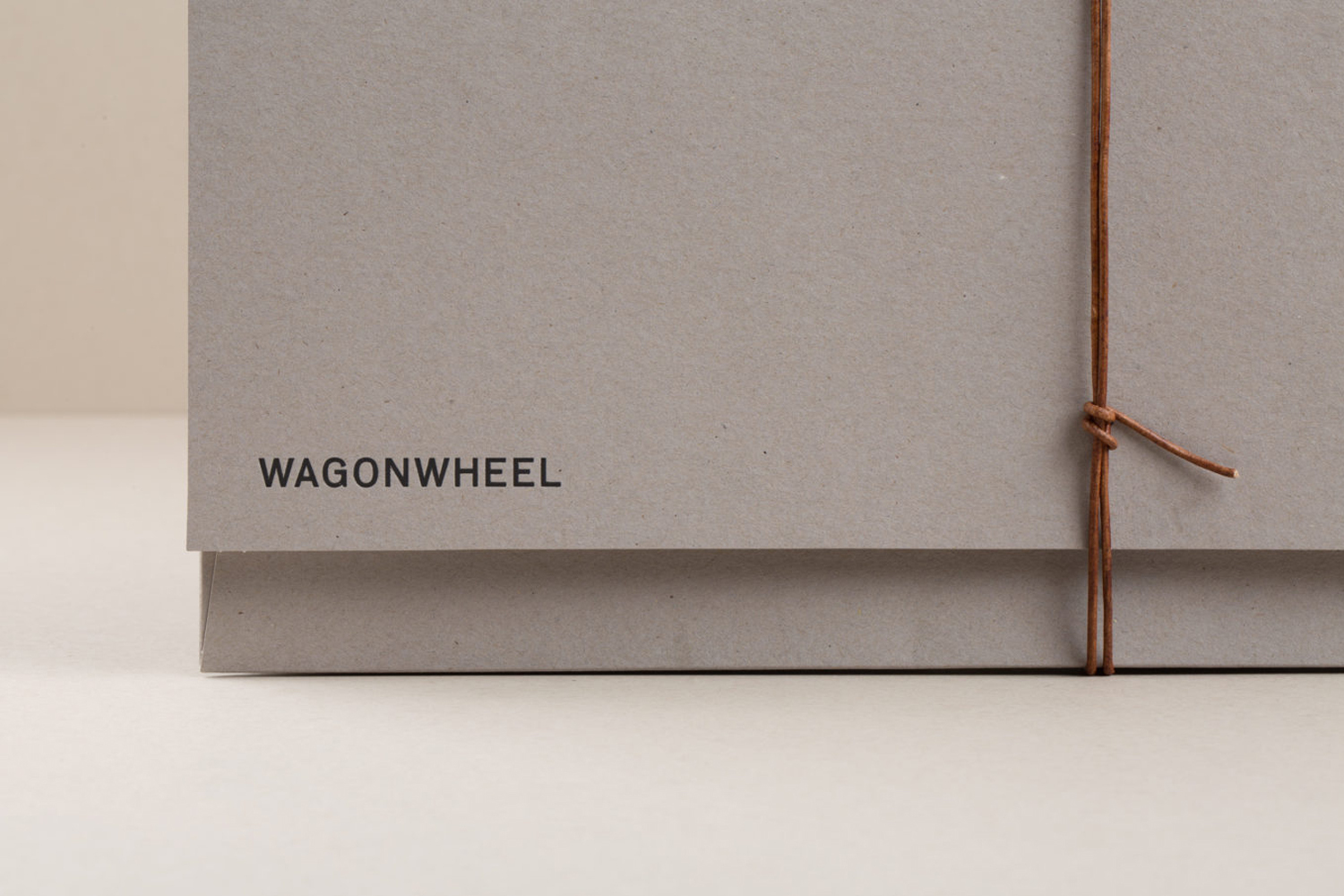 Tan kraft paper box with the text "WAGONWHEEL" printed in dark gray on the upper left side, tied with brown suede string.