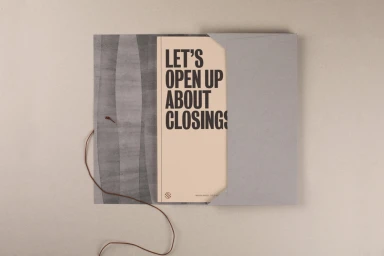 Open grey paper envelope containing a cream booklet with bold dark lettering that reads lets open up about closings