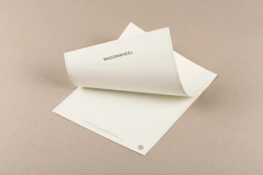 A stack of cream-colored stationery featuring the Wagon Wheel brand name on a textured grey background