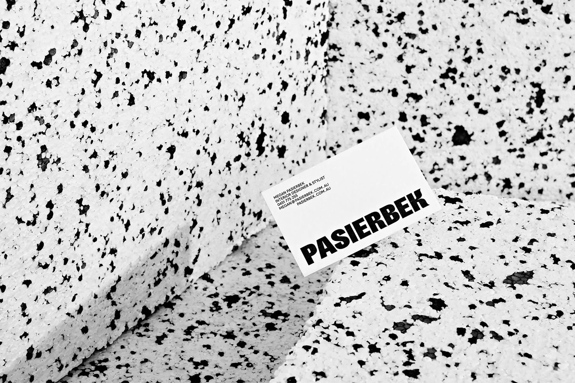 Close-up of a business card for Pasierbek Interior Designer & Stylist resting on a textured surface of white with black specks.