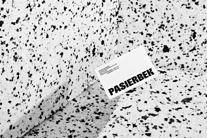 Close-up of a business card for Pasierbek Interior Designer & Stylist resting on a textured surface of white with black specks.
