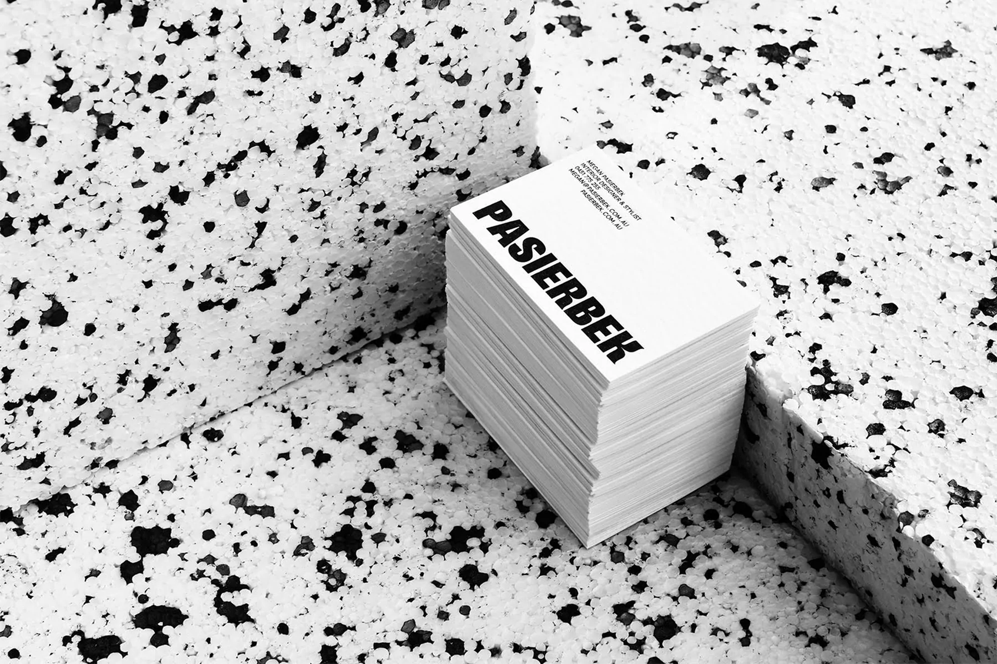 Stack of white business cards with the name 'PASIERBEK' in bold black text, set against a textured white and black background.