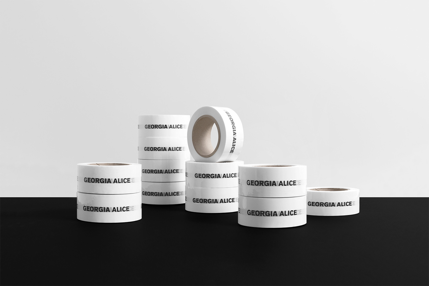 Several stacks and rolls of white tape with black text sit on a black surface against a graduated white background in a product shot.