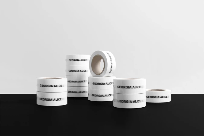 Several stacks and rolls of white tape with black text sit on a black surface against a graduated white background in a product shot.