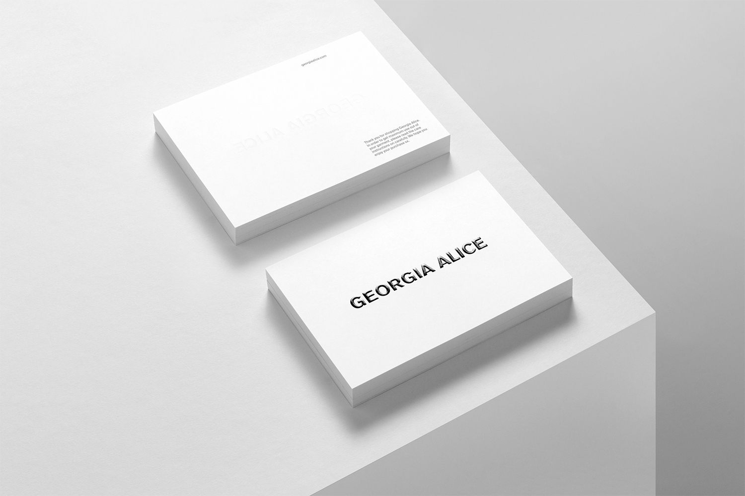 Two stacks of white business cards on a white geometric background in a minimalist design, featuring the name Georgia Alice.