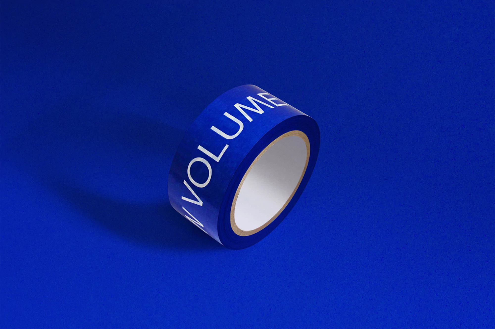 Roll of blue tape with white text on a bright blue backdrop creates a minimalist, studio product shot with sharp shadows.