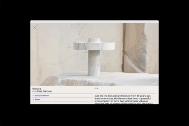 A white marble desk lamp resting on a rough stone surface against a textured background, presented in a website interface.