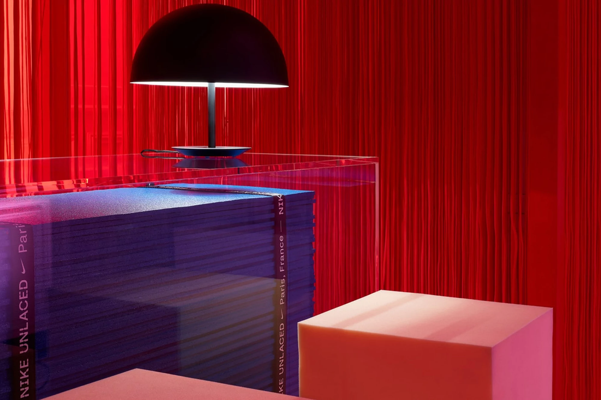 A black dome lamp sits on a stack of blue boxes with red drapery in the background and red and pink podiums in the foreground.