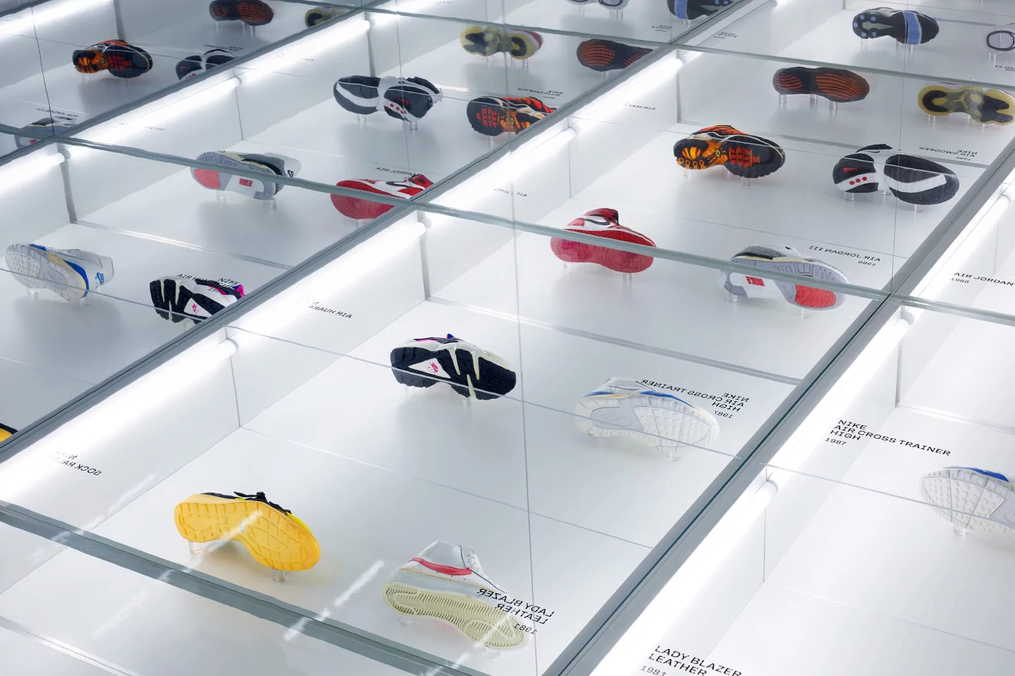 Array of colorful vintage athletic shoes displayed in illuminated glass display cases. Shoes are individually presented with labels.