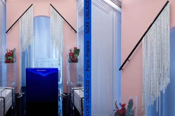 A visually striking Nike product display featuring reflective fringe, floral arrangements, clear acrylic stands, and bold textual branding in a modern setting.