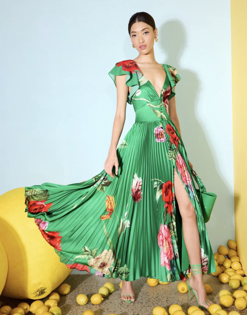 Woman in green floral dress stands among lemons in a studio setting, posing for a fashion editorial, showcasing a summer collection.