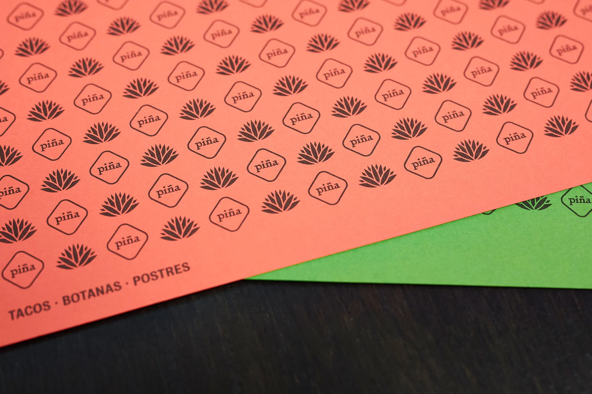 Overhead shot of diagonally overlapping sheets of colorful menu paper printed with brand logos and restaurant categories like tacos and postres.