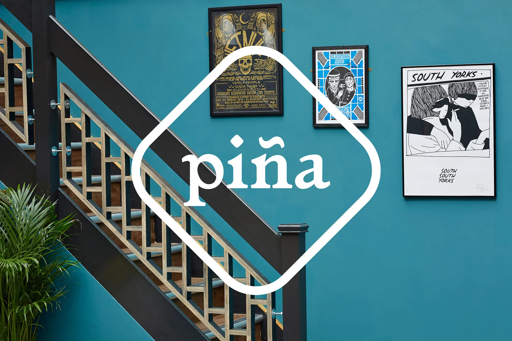 Indoor shot of an interior wall with graphic art, a staircase with handrail, and a leafy plant, creating a visually appealing and modern design.