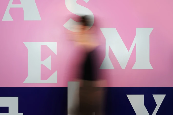 Motion blur of a person in front of a pink wall with white letters and a dark blue band at the bottom, creating an abstract effect.