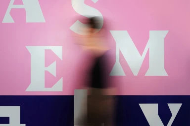 Motion-blurred person walking past a pink and blue wall with large white serif typography for Assembly brand identity.