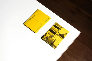 Two stacks of bright yellow postcards featuring black typography and graphic illustrations resting on a white table.