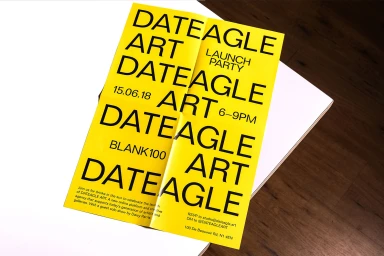 Bright yellow folded poster with bold black typography resting on a white and wood surface