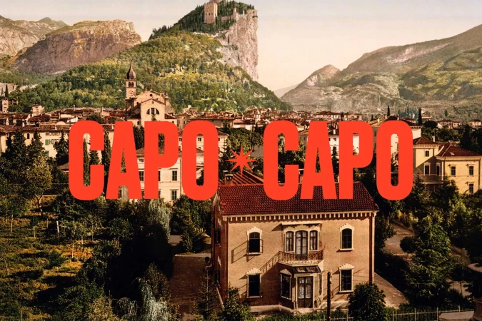 Cityscape of Arco, Italy with mountains, trees and houses beneath a large red text overlay reading 'CAPO CAPO'.