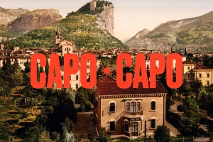 Vintage landscape view featuring a town nestled in a valley with mountains and a bold red typographic overlay reading CAPO
