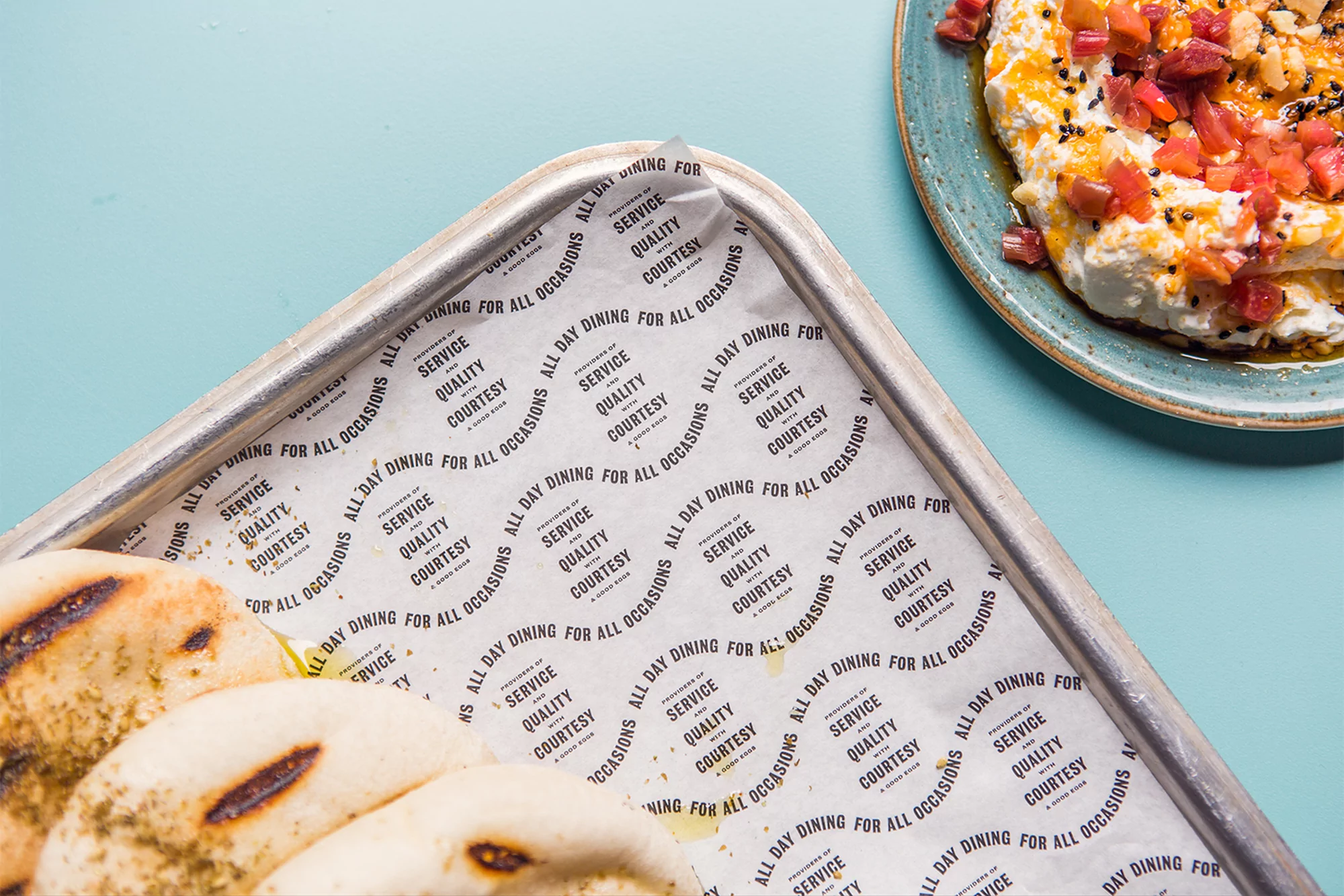 Overhead shot of a plate of labneh dip and a tray of flatbreads on a light blue table, highlighting healthy Mediterranean cuisine.