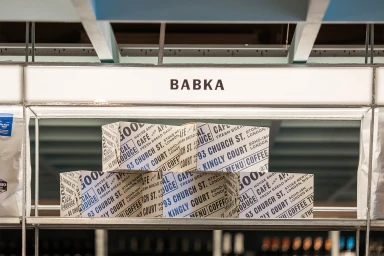 Branded food packaging boxes with blue and black typography on shelves beneath an illuminated sign reading BABKA.