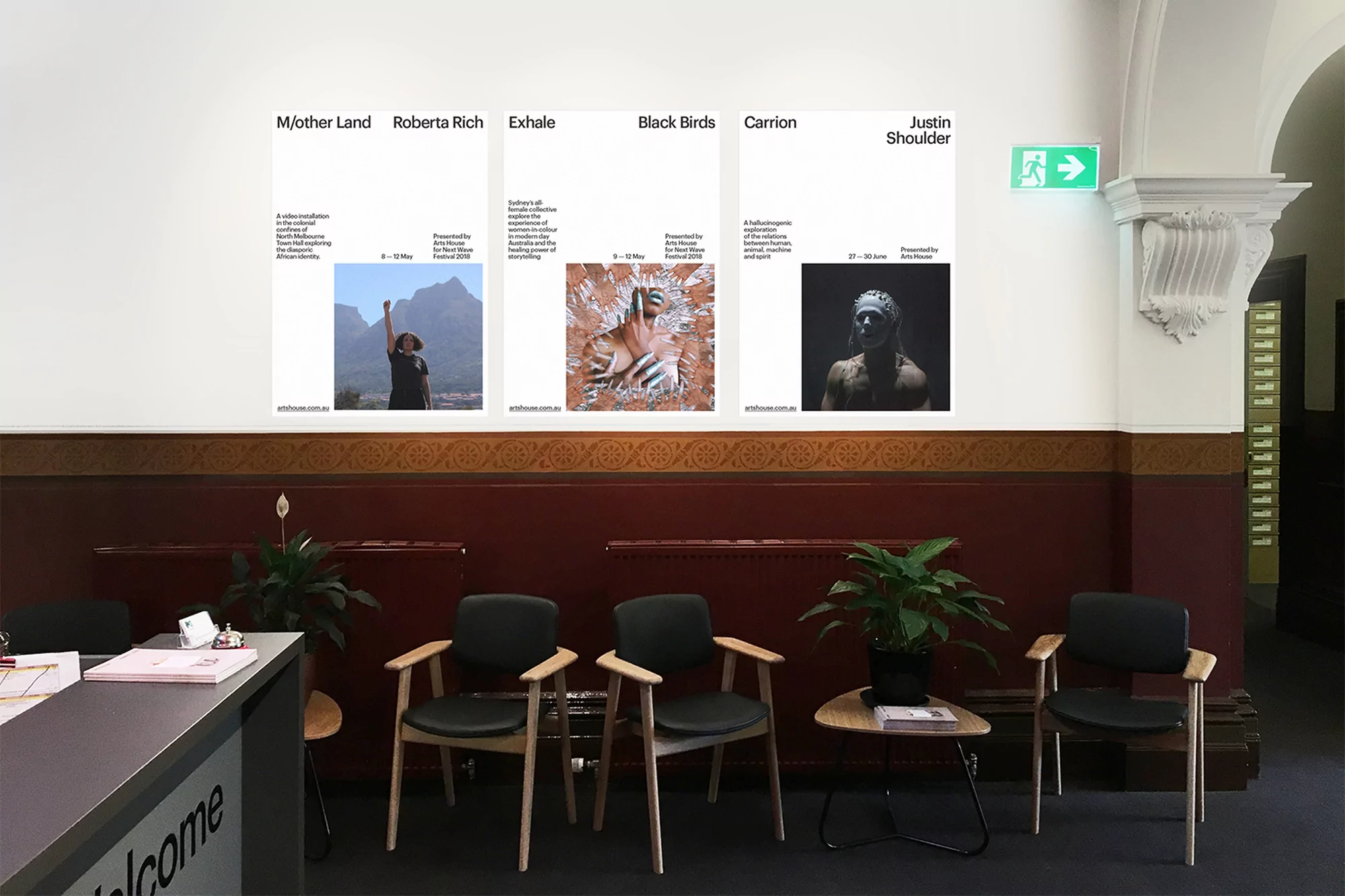 A waiting area with black chairs faces five art posters with images, showcasing a modern gallery exhibit in a well-lit interior space.