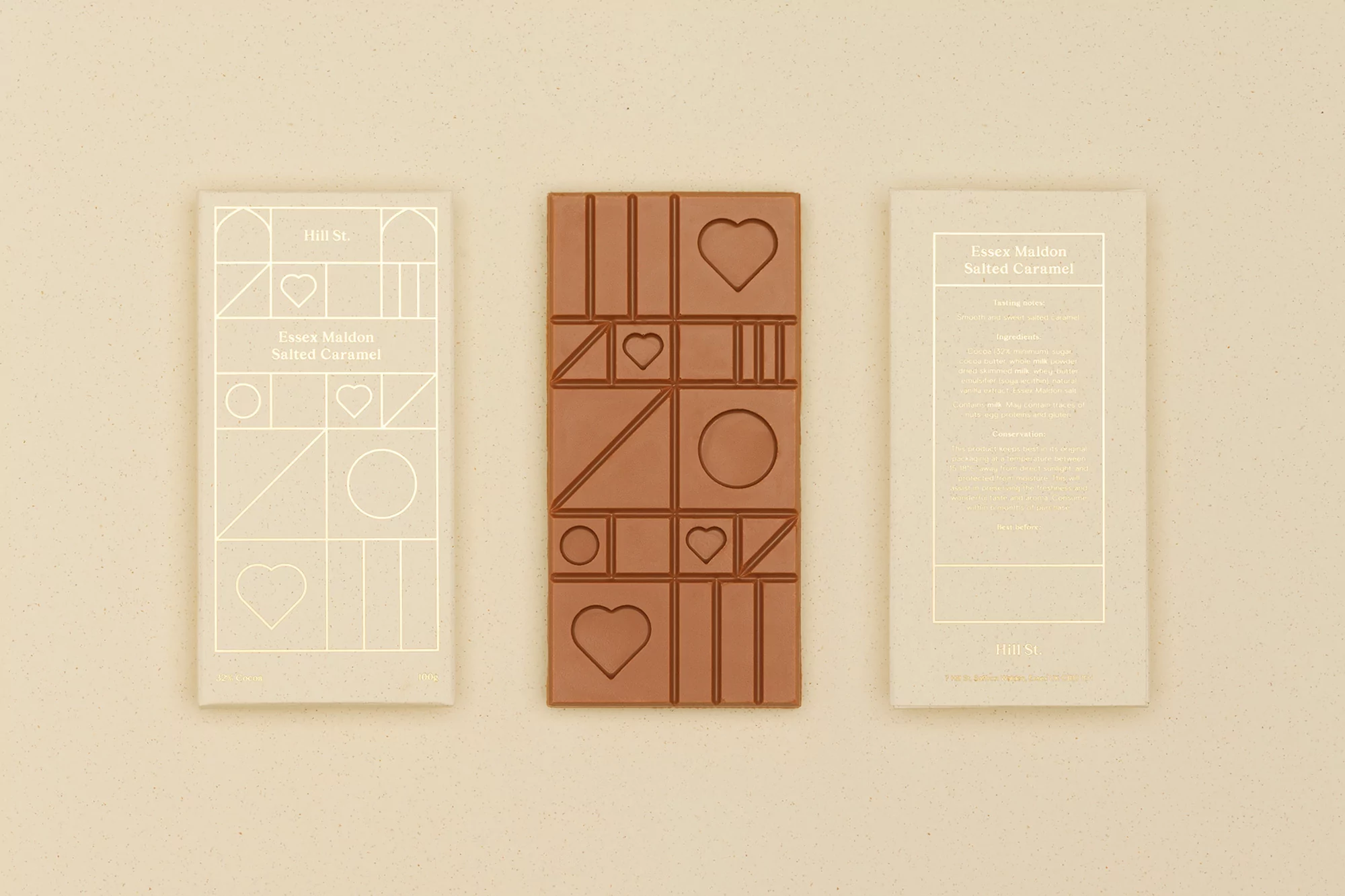 Milk chocolate bar and wrappers with geometric, heart, and circle shapes, styled on a cream-colored surface, food photography.