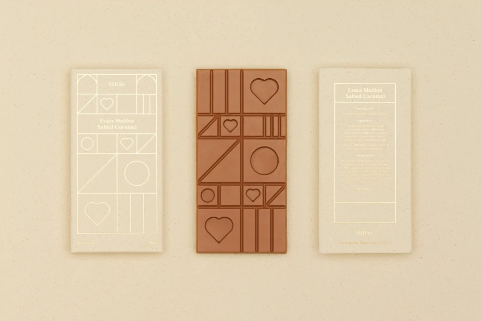 Milk chocolate bar and wrappers with geometric, heart, and circle shapes, styled on a cream-colored surface, food photography.