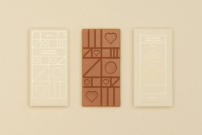 Milk chocolate bar and wrappers with geometric, heart, and circle shapes, styled on a cream-colored surface, food photography.