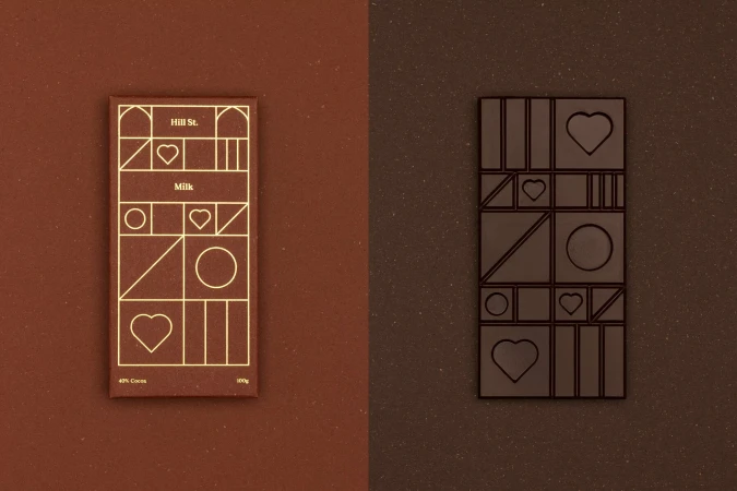 Two milk chocolate bars, one with gold graphic geometric design, the other with geometric chocolate pieces, on brown backgrounds.