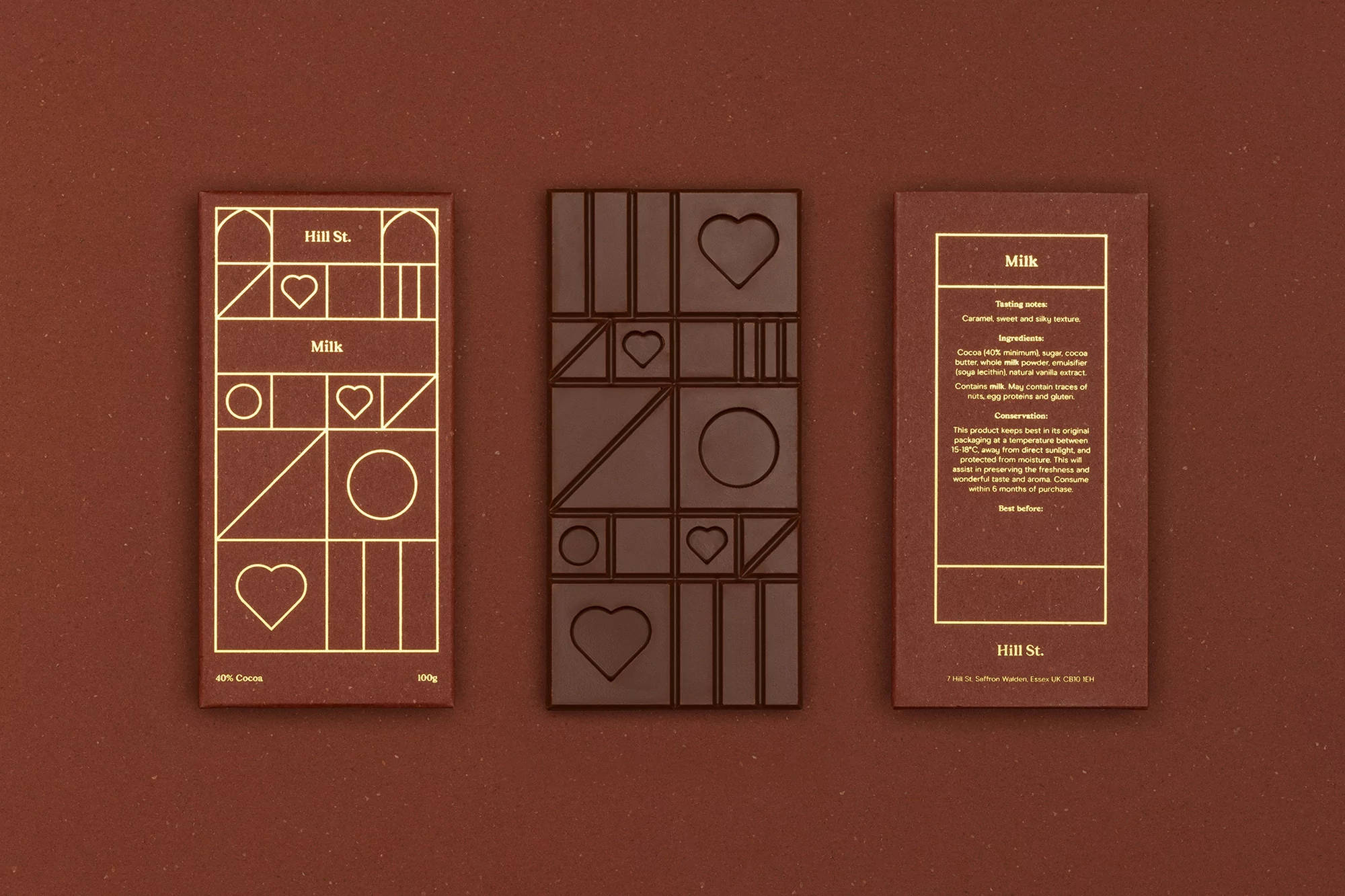 Still life of three Hill St. milk chocolate bars on a brown background, displaying geometric line art and heart shape details on the packaging.