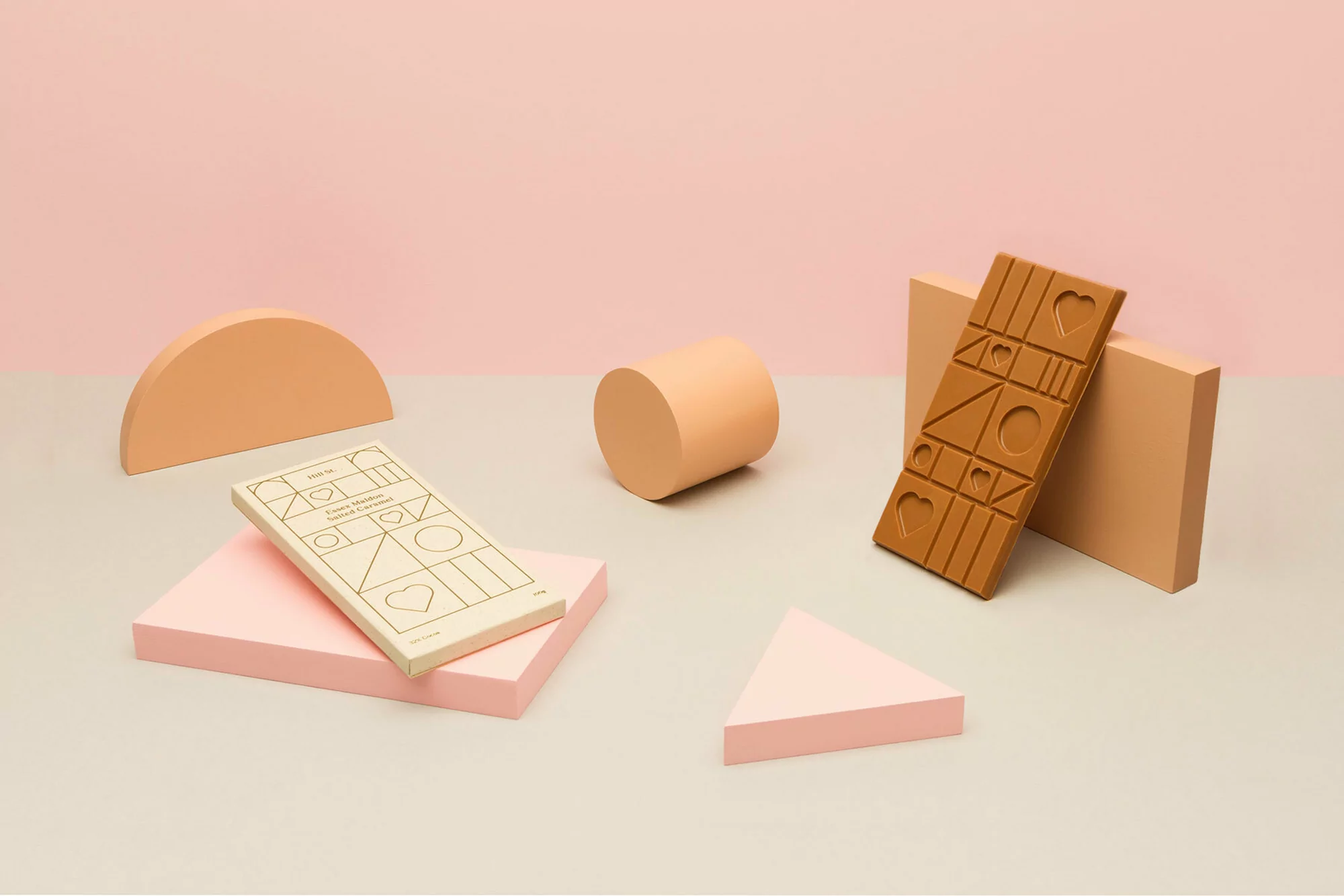 Still life photo of a chocolate bar and geometric shapes in pastel colors against a pink backdrop for food and product photography.