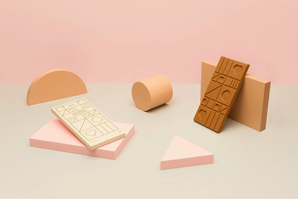 Still life photo of a chocolate bar and geometric shapes in pastel colors against a pink backdrop for food and product photography.