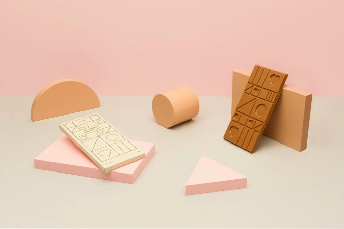 Still life photo of a chocolate bar and geometric shapes in pastel colors against a pink backdrop for food and product photography.