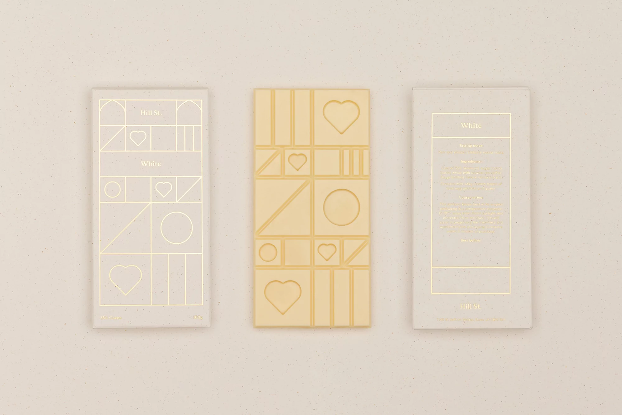 Three bars of white chocolate arranged in a horizontal row on a light beige surface, featuring geometric patterns and minimalist design.