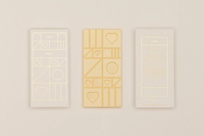 Three bars of white chocolate arranged in a horizontal row on a light beige surface, featuring geometric patterns and minimalist design.