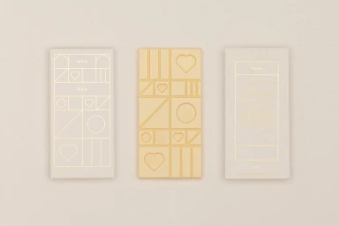 Three chocolate bars by Hill St with geometric patterns and gold foil packaging against a neutral background.