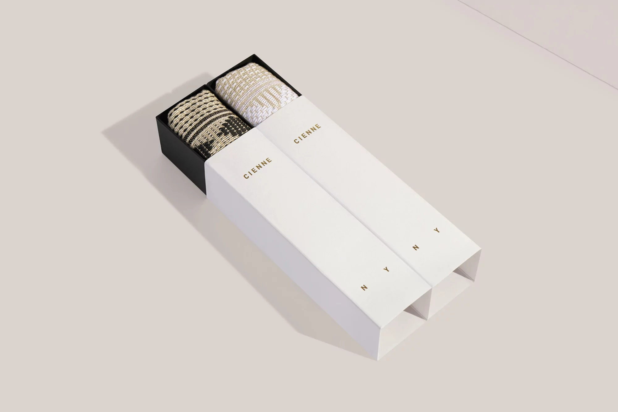 Two boxes from Cienne NY containing woven textiles sit on a beige surface with bright, even lighting and sharp focus.